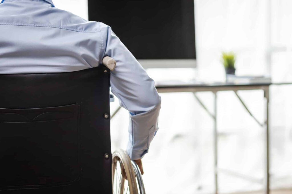 Man in wheelchair working with computer on desk in office.