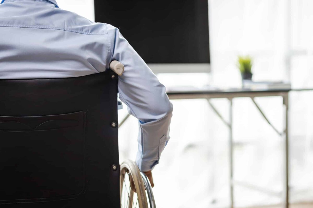 Man in wheelchair working with computer on desk in office.