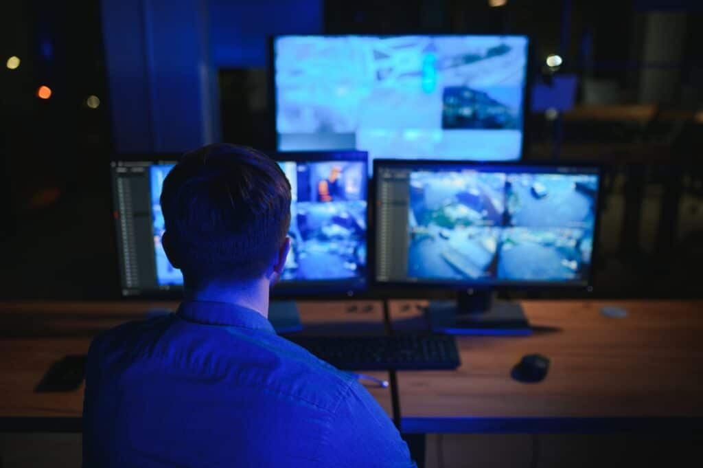 Rear view of security system operator looking at CCTV footage at desk in office