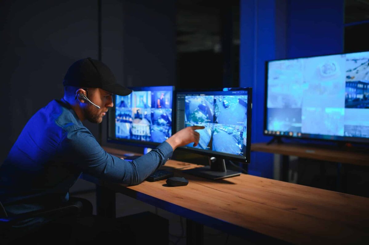 Rear view of security system operator looking at CCTV footage at desk in office