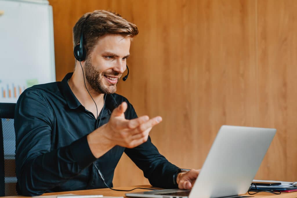 Young caucasian man in headset explaining emotionally sitting in front of laptop computer.