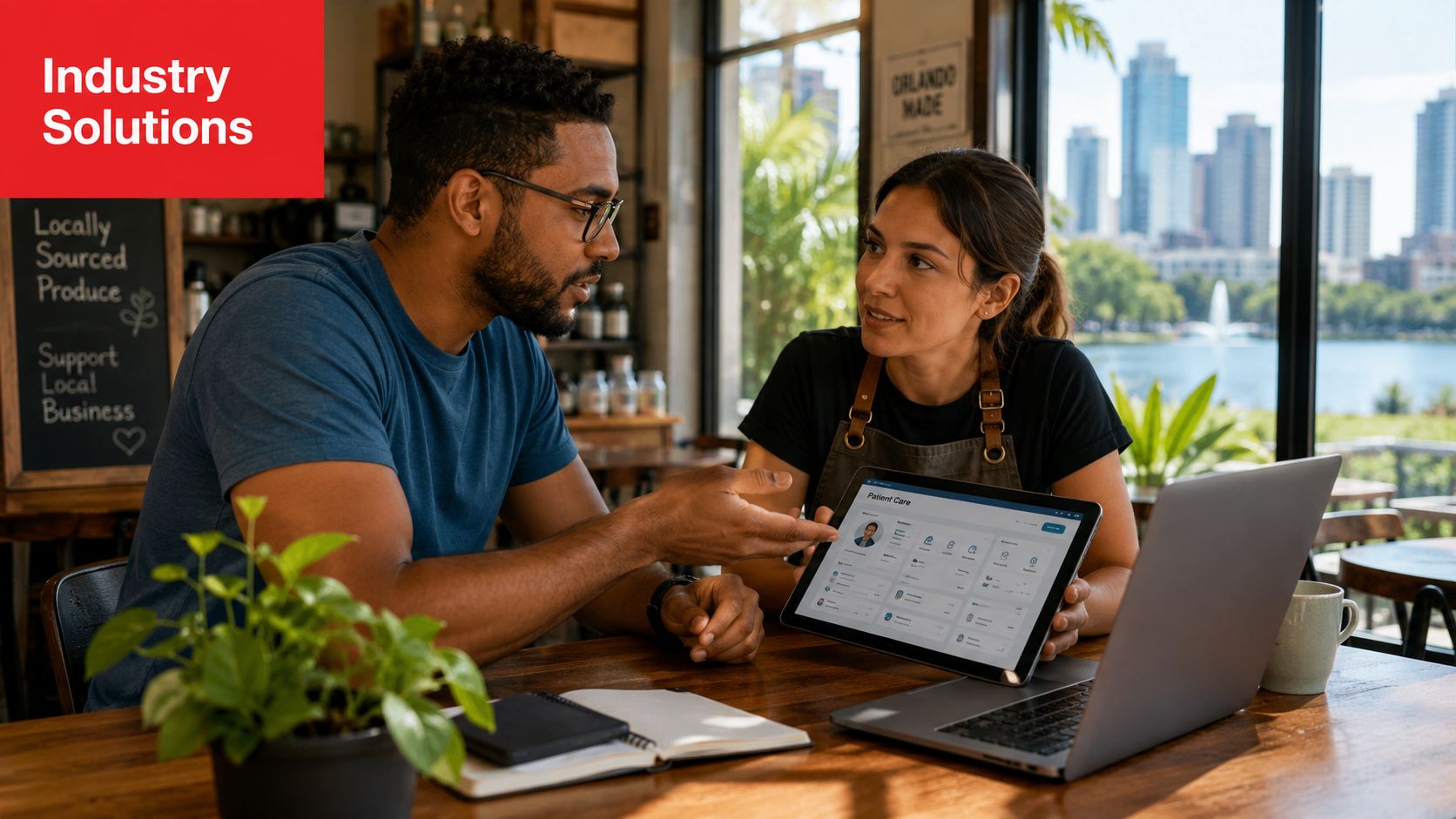 A professional man and woman discussing IT solutions on a tablet computer in a modern coffee shop.